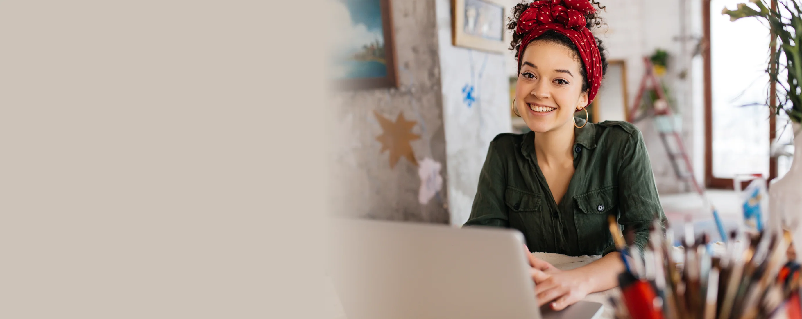 Mujer sonriente con pañoleta roja trabajando en un laptop en su estudio